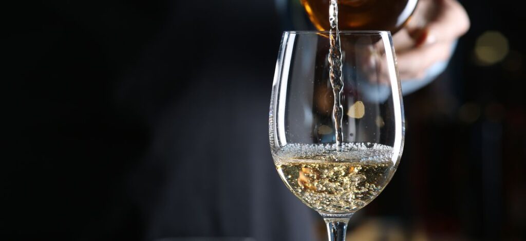 Bartender pouring white wine from bottle into glass indoors, closeup. 